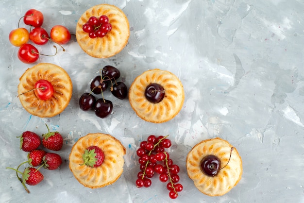 A top view yummy cakes with mellow and juicy red fruits on the light desk berry fruit cake sugar cake