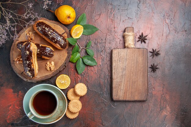 Top view yummy choco eclairs with cup of tea on dark table dessert sweet cake