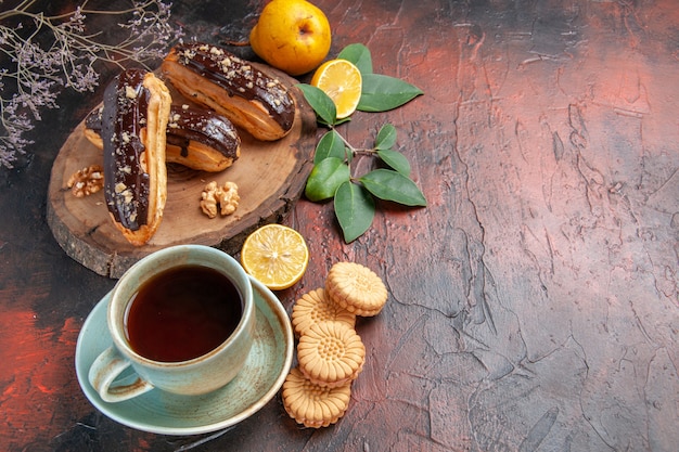 Top view yummy choco eclairs with cup of tea on the dark table dessert sweet cake