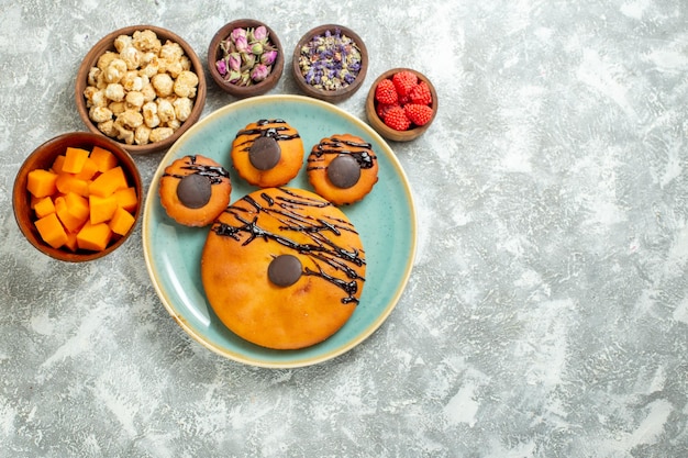 Top view yummy cocoa cakes with chocolate icing and flowers on white surface biscuit sweet cake dessert cookie pie