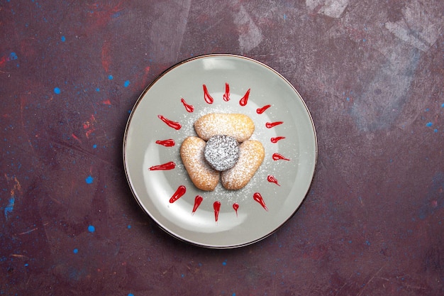 Top view of yummy cookies with sugar powder and red icing inside plate on dark