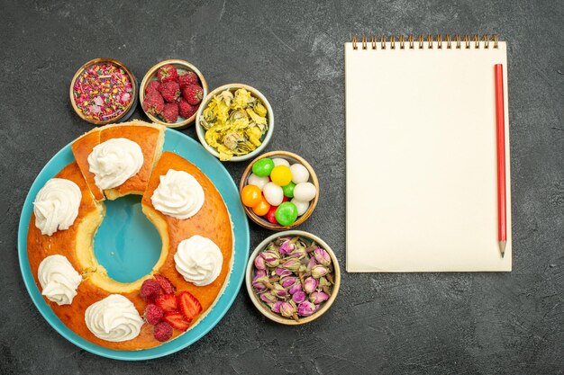 Top view of yummy cream pie with flowers and candies on black