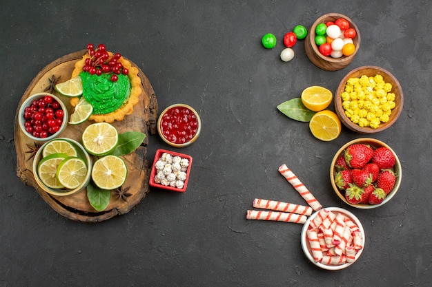 Top view yummy creamy cake with candies and fruits on the dark background sweet cookie biscuit