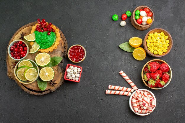 Top view yummy creamy cake with candies and fruits on the dark background sweet cookie biscuit