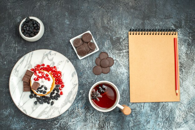 Top view yummy creamy cake with choco biscuits and cup of tea on a light-dark background