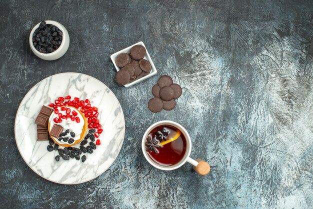 Top view yummy creamy cake with choco biscuits and cup of tea on light-dark background