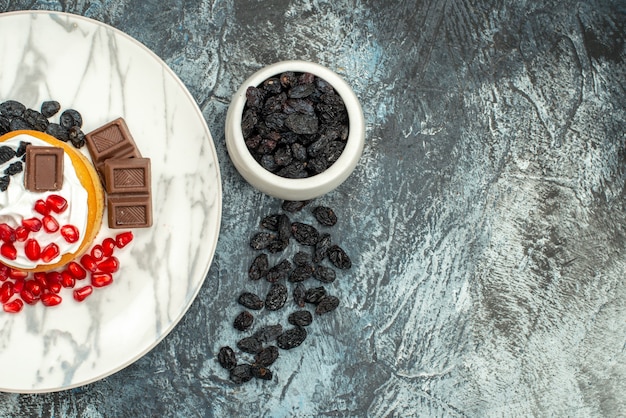 Free photo top view yummy creamy cake with chocolate pomegranates and raisins on light-dark background