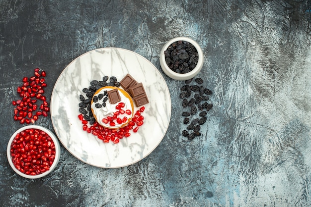 Free photo top view yummy creamy cake with chocolate pomegranates and raisins on light-dark background