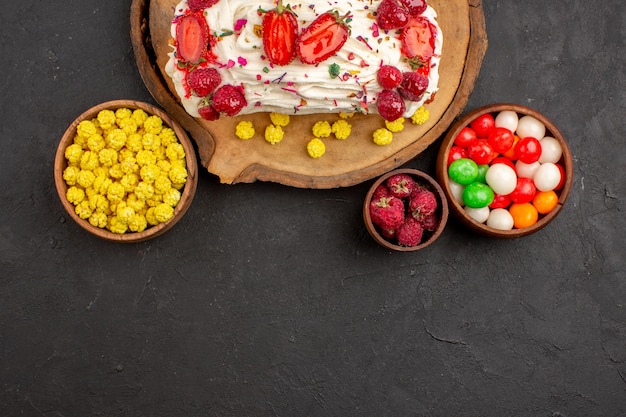 Free photo top view of yummy creamy cake with fruits and candies on black