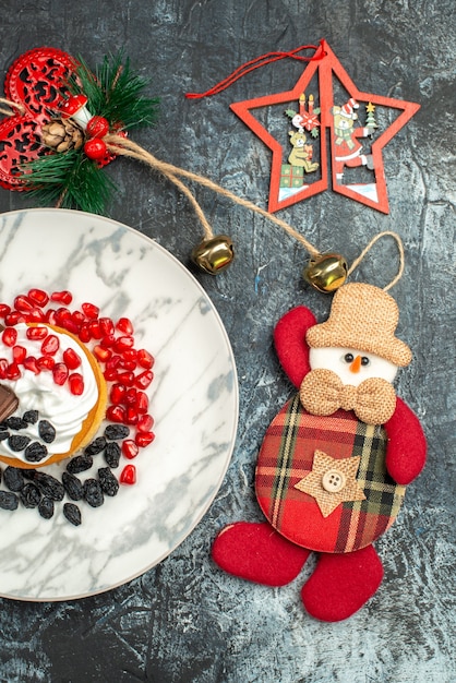 Top view yummy creamy cake with raisins and christmas toys on light-dark background