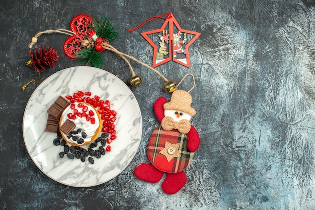 Top view yummy creamy cake with raisins and christmas toys on light-dark background