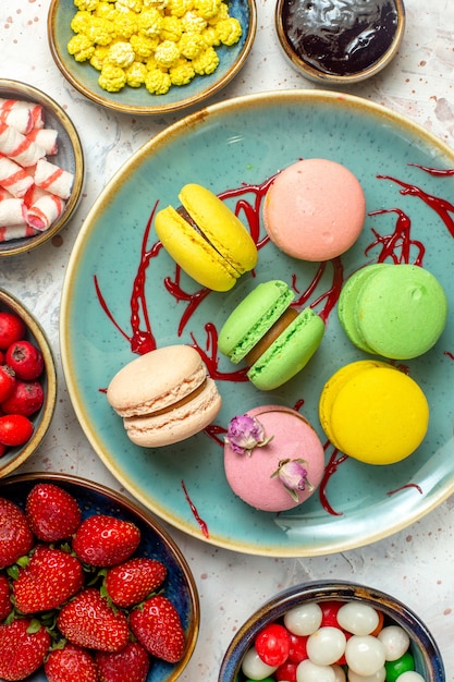 Top view yummy french macarons with berries and candies on a white cake sweet biscuit