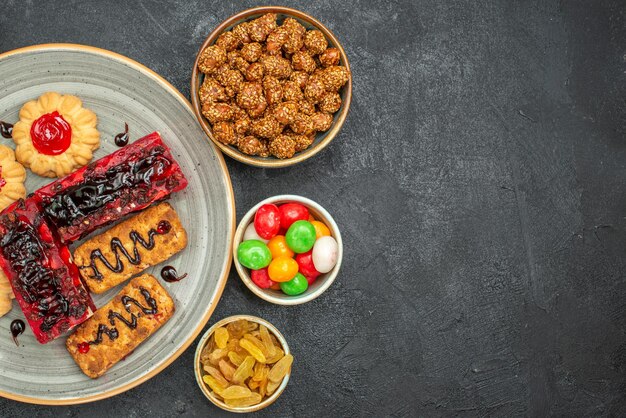 Top view of yummy fruity cakes with cookies and candies on dark