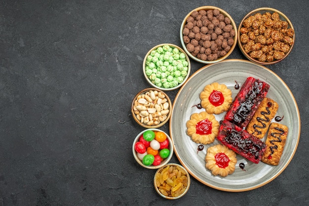 Top view of yummy fruity cakes with nuts and candies on grey