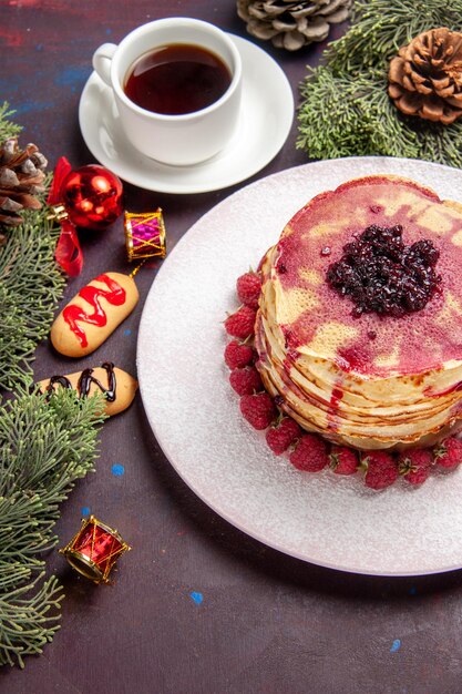 Top view of yummy fruity pancakes with cup of tea on dark