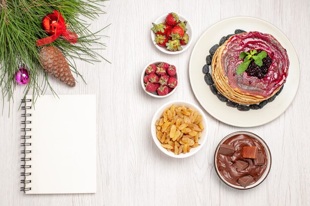 Top view yummy jelly pancakes with raisins and fruits on white