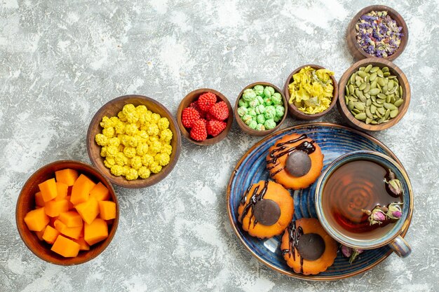 Top view yummy little cakes with cup of tea and candies on white surface cake biscuit cookie dessert sweet tea