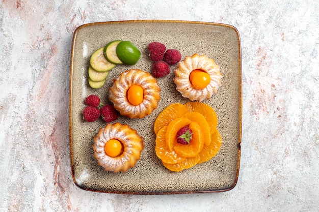 Free photo top view of yummy little cakes with sliced fruits on white