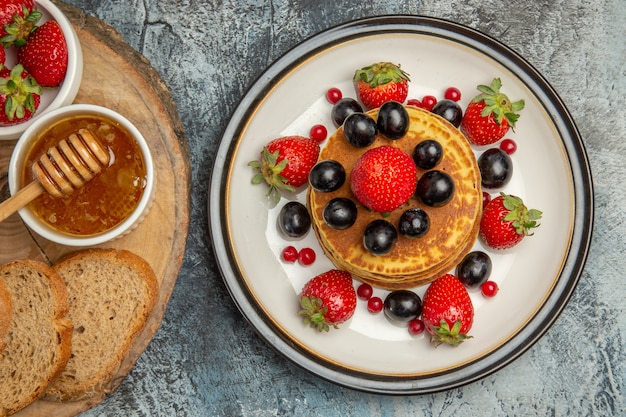 Top view yummy pancakes with fresh fruits and bread on light floor fruit cake sweet