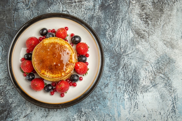 Top view yummy pancakes with fruits and honey on light floor