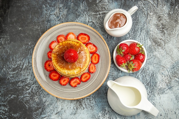 Top view yummy pancakes with honey and strawberries on light