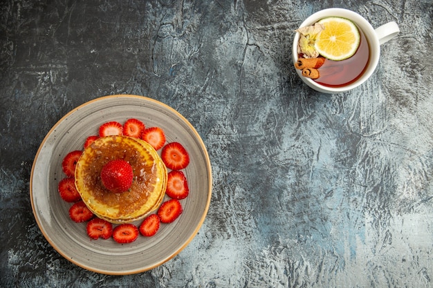 Top view yummy pancakes with strawberries and cup of tea on light