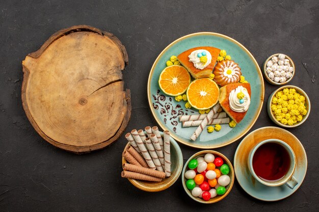 Top view yummy pie slices with fresh tangerines tea and candies on dark