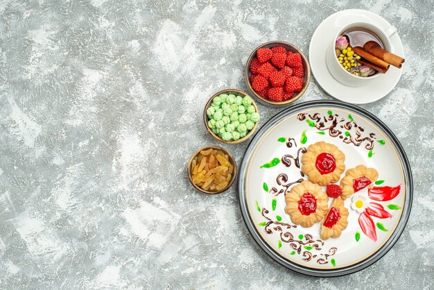 Top view yummy sweet cookies with candies and cup of tea on white