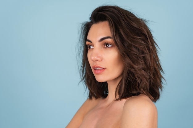 Topless beauty portrait of a young woman with bare shoulders and light natural make-up, with short wavy hair, retouched, on a light blue background