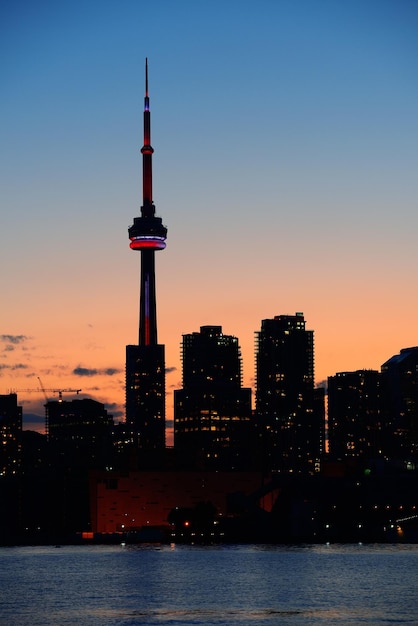 Toronto city skyline silhouette at sunset over lake with urban skyscrapers.