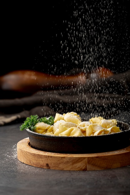 Free photo tortellini in dark metallic plate on a wooden stand