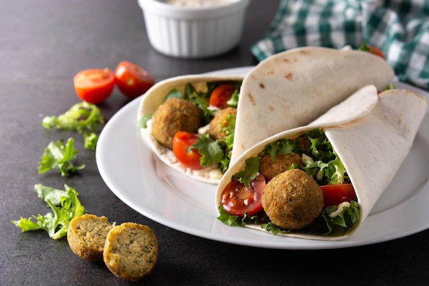 Free Photo tortilla wrap with falafel and vegetables on black stone background