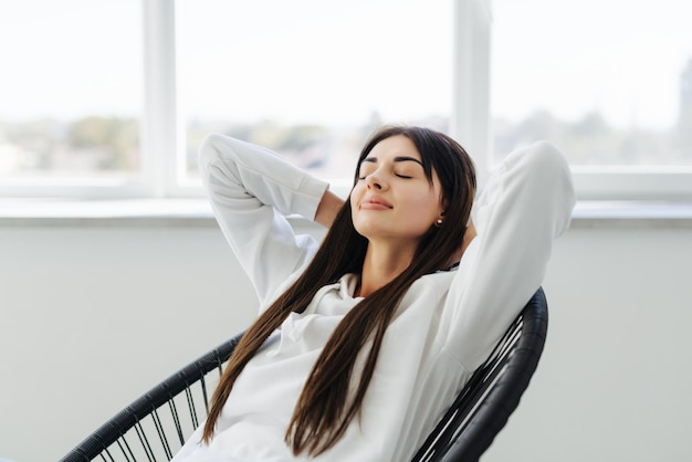 Free photo total relaxation attractive young woman holding hands behind head and smiling while sitting at the chair at home