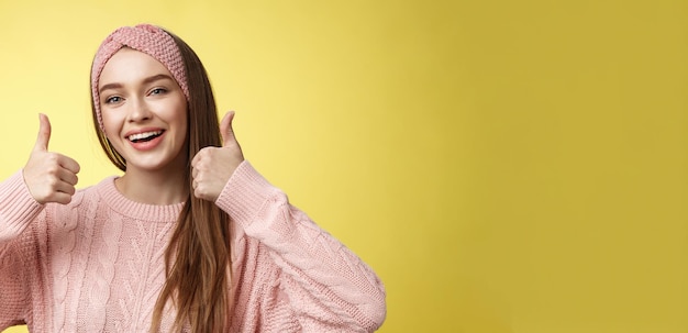 Free photo totally approve girl agrees taking part in interesting activity smiling joyful staying positive showing thumbs up in support recommend super cool service posing delighted against yellow wall