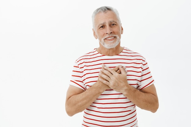 Touched and happy, flattered senior man holding hands on heart and smiling