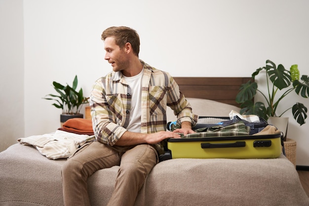 Free photo tourism and travelling concept portrait of handsome young man going on holiday packing his suitcase