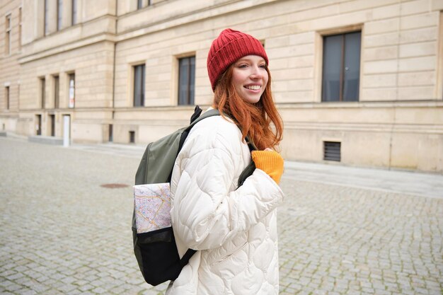 Tourism and travelling young redhead woman smiling tourist walking with backpack around city centre