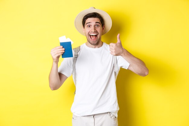 Tourism and vacation. Satisfied male tourist showing passport with tickets and thumb up, recommending travel company, standing over yellow background.