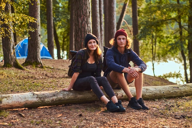 Free Photo tourist girl holds hand on chin while sitting on a tree trunk and holds a smartphone in the forest.