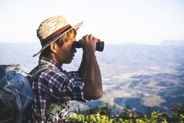 Tourist is watching through binoculars on sunny cloudy sky from mountain top. 