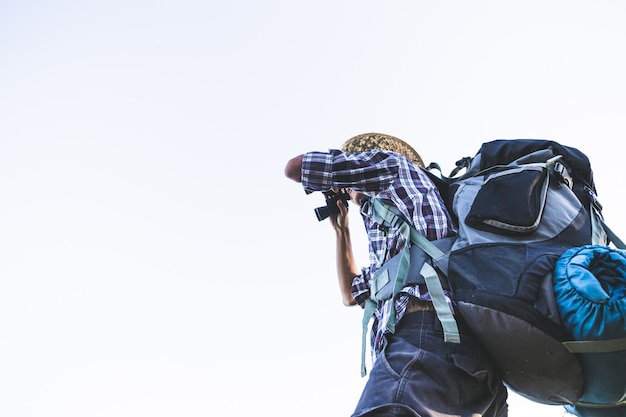 Tourist is watching through binoculars on sunny cloudy sky from mountain top. 