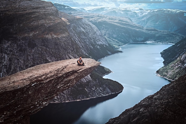 Free Photo tourist man sitting in the trolltunga and enjoys the beautiful view of the norwegian fjord.