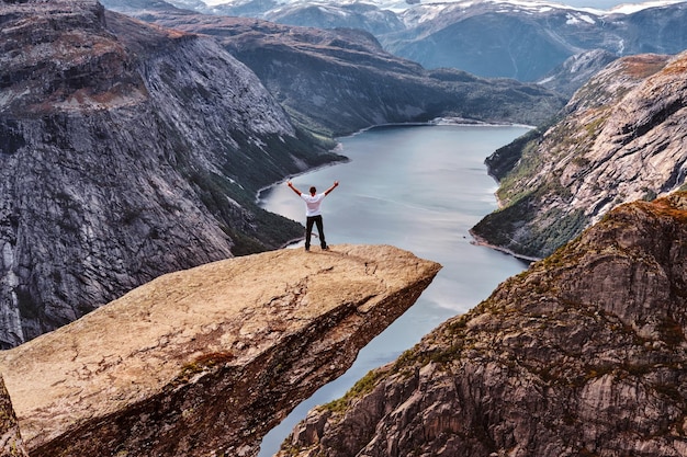 Tourist man standing in the Trolltunga and enjoys the beautiful view of the Norwegian fjord.