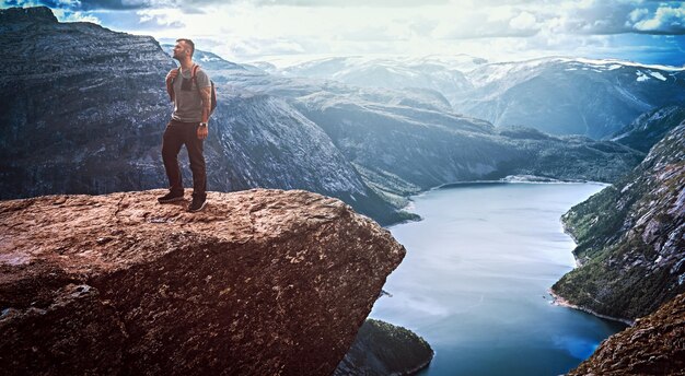 Tourist man standing in the Trolltunga and enjoys the beautiful view of the Norwegian fjord.