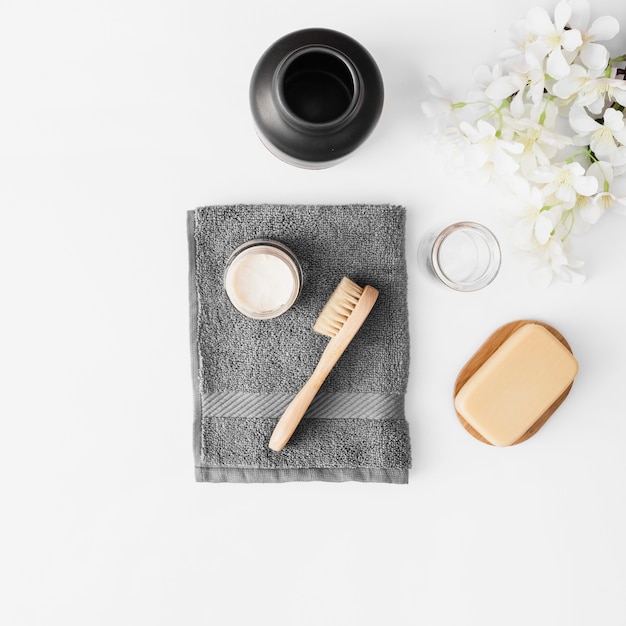 Towel; brush; moisturizing cream; soap; jar and flowers on white surface