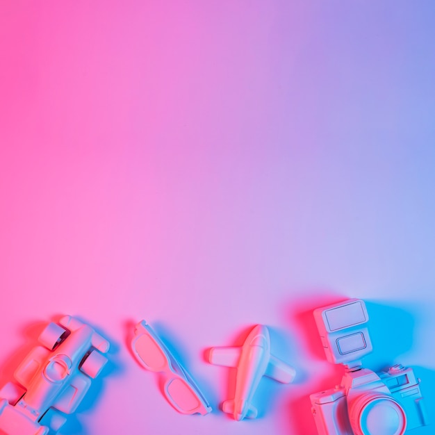 Free photo toy car; plane; spectacle and camera arranged at the bottom of pink background with blue light