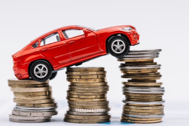 Free photo toy red car over the stack of increasing coins against white background