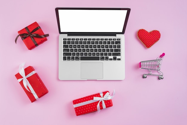 Toy shopping trolley and heart near laptop and gifts