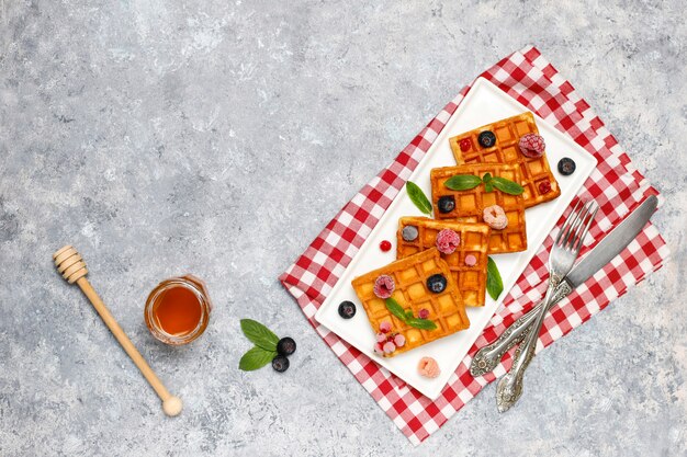 Traditional belgian waffles with fresh berries and honey on grey concrete surface. 