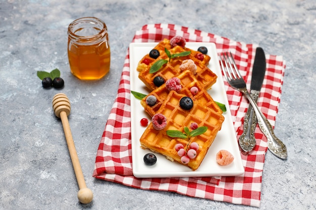 Free photo traditional belgian waffles with fresh berries and honey on grey concrete surface.